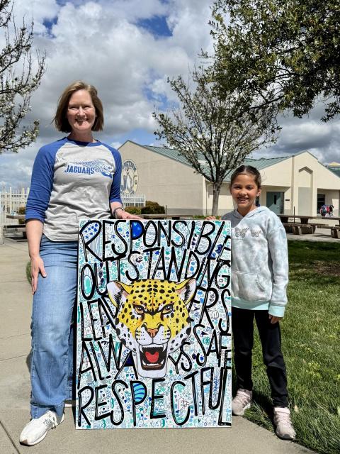 Mrs. Mochrie and student standing in front of school. In between them is a large painting of a jaguar. 